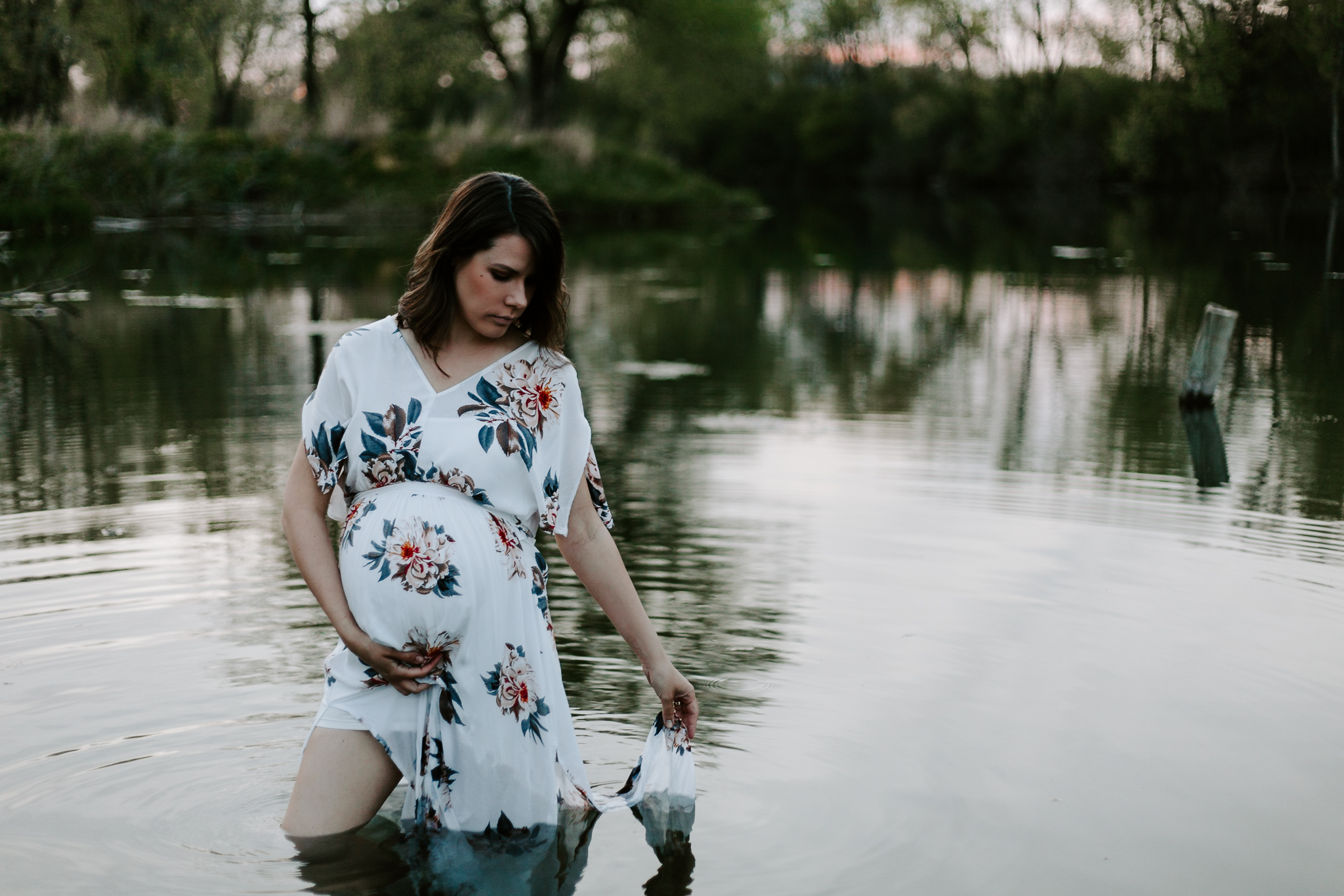 Expecing mother in a floral maxi dress wading in pond at blue hour.